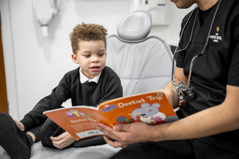 Dentist putting a child sat in the treatment chair at ease by reading him a book